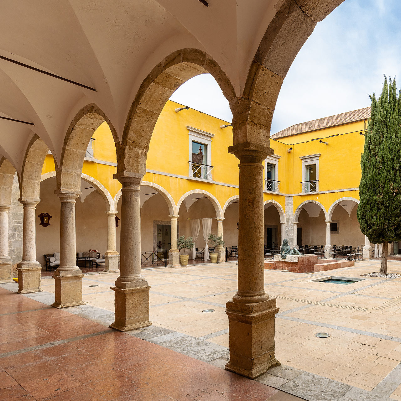 Cloister of Pousada Convento Tavira, a historical hotel in Tavira, with a statue in the center and a tree