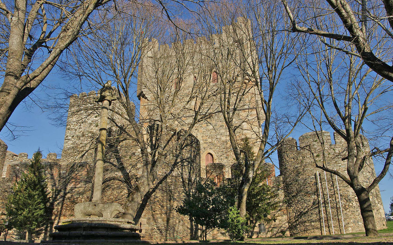 Exterior view of the castle of Pousada Bragança, with trees and leaves in front of the façade of the inn
