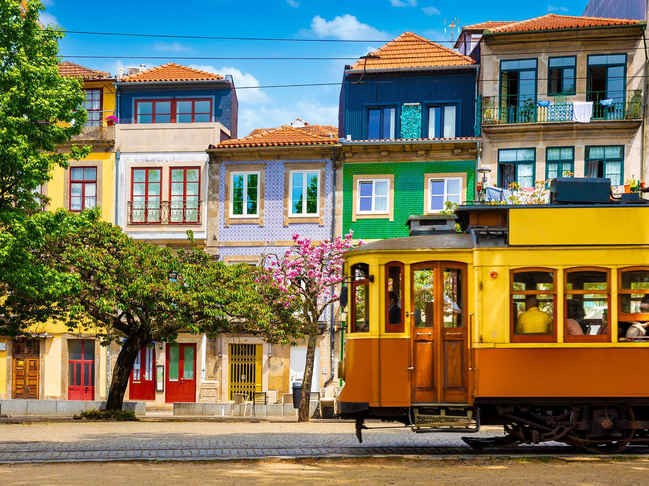 Explore Hotels in Porto featuring a yellow tram passing colourful tiled houses beneath a bright blue sky