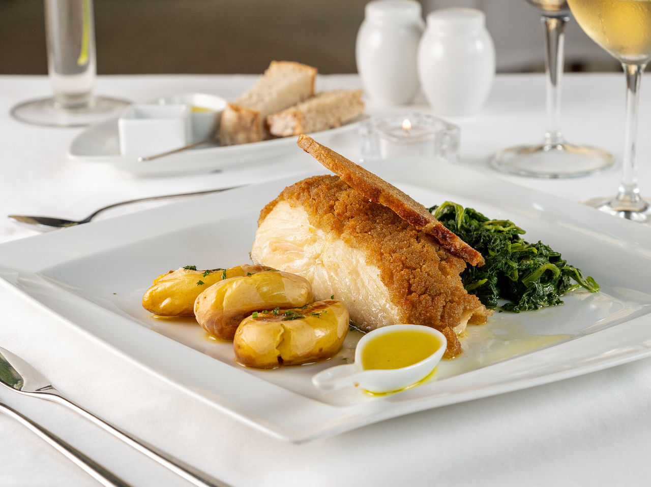 Discover Pousadas de Portugal featuring a plated fish dish with potatoes, greens and wine on a white table